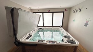 Ein Whirlpool mit Holzunterbau, einer Bedienkonsole und einem Fenster darüber.