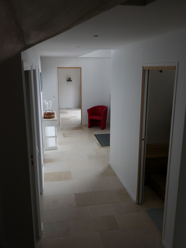 A narrow hallway with a red chair, a small table with a basket, and a door leading to another room.