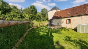 Ein Steinhaus mit rotem Ziegeldach, einem Holzzaun und einem grünen Schuppen.