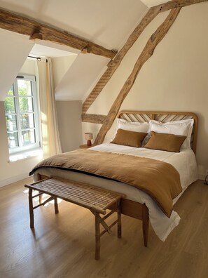 Un dormitorio con techo de madera, una cama con cabecera, una mesita de noche y un ventanal con cortinas.