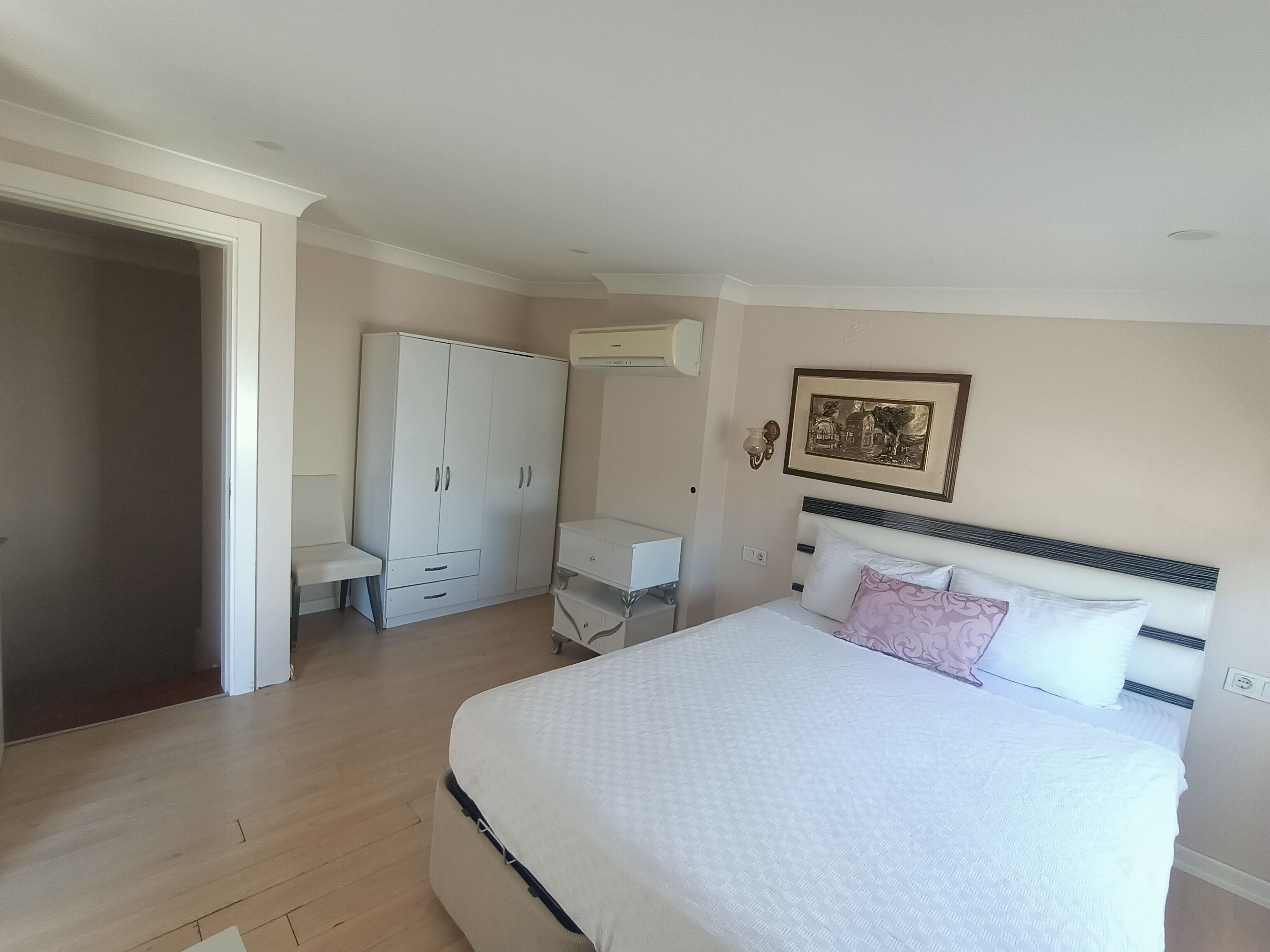 Un dormitorio con una cama grande, un armario, un escritorio y un aire acondicionado instalado en la pared.