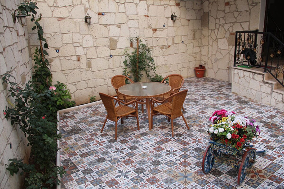 A courtyard with a round table and chairs, a tiled floor, a potted plant, and a flower cart.