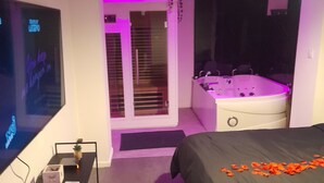 A modern bedroom with a large bed, a TV, a desk with a laptop, a bathtub, and a shower area. - le spa d Ailly (Ailly-sur-Somme)