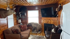 A cabin interior with wooden walls, a brown couch, a television, and mounted animal heads. - Cozy Cabin with beautiful view of Lake Michigan. Pet Friendly (Rapid River)