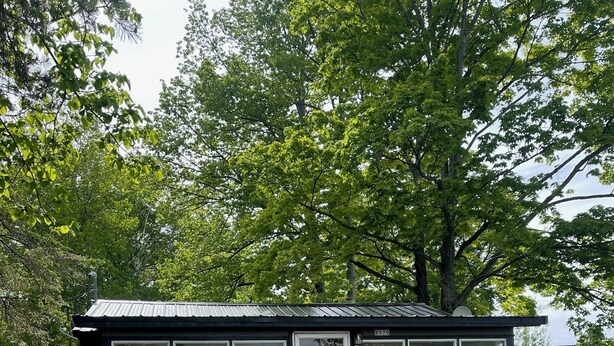 A small, single-story building with a dark exterior and white-framed windows. It features a front entrance with a set of stairs leading up to a door. - Cozy Cabin with beautiful view of Lake Michigan. Pet Friendly (Rapid River)