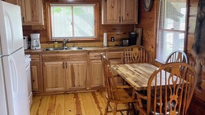 A wooden cabin interior with a kitchen, dining area, and a clock on the wall. - Cozy Cabin with beautiful view of Lake Michigan. Pet Friendly (Rapid River)