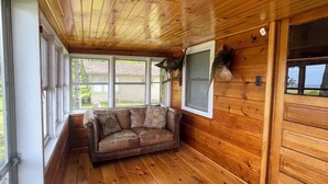 A cozy cabin interior with a wooden ceiling, a leather sofa, and a large window. - Cozy Cabin with beautiful view of Lake Michigan. Pet Friendly (Rapid River)