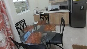 Une cuisine de taille réduite comprenant une table à manger, des chaises, un réfrigérateur et une fenêtre avec des rideaux.