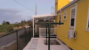 Un bâtiment jaune avec une structure métallique noire, qui pourrait être une salle de sport ou un espace d’exercice en plein air, et une clôture blanche.