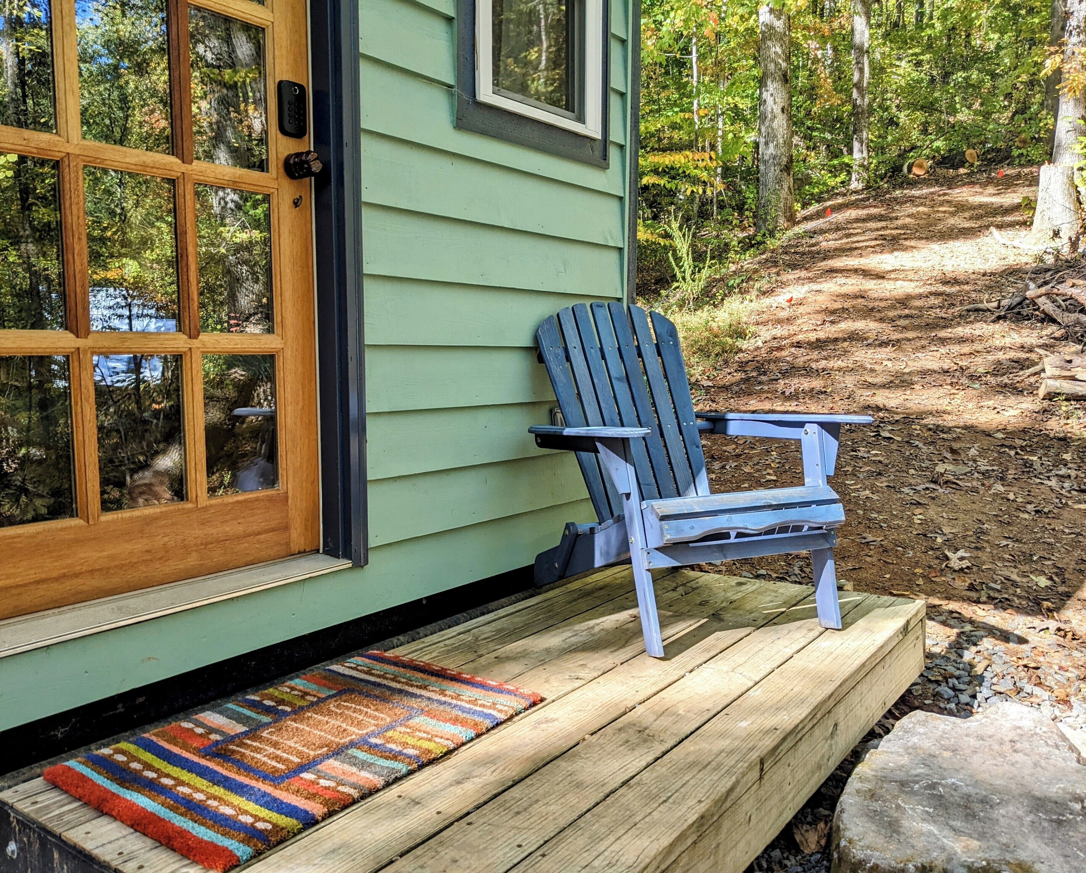 Una terraza de madera con una silla Adirondack azul, un tapete colorido y una puerta con ventana.
