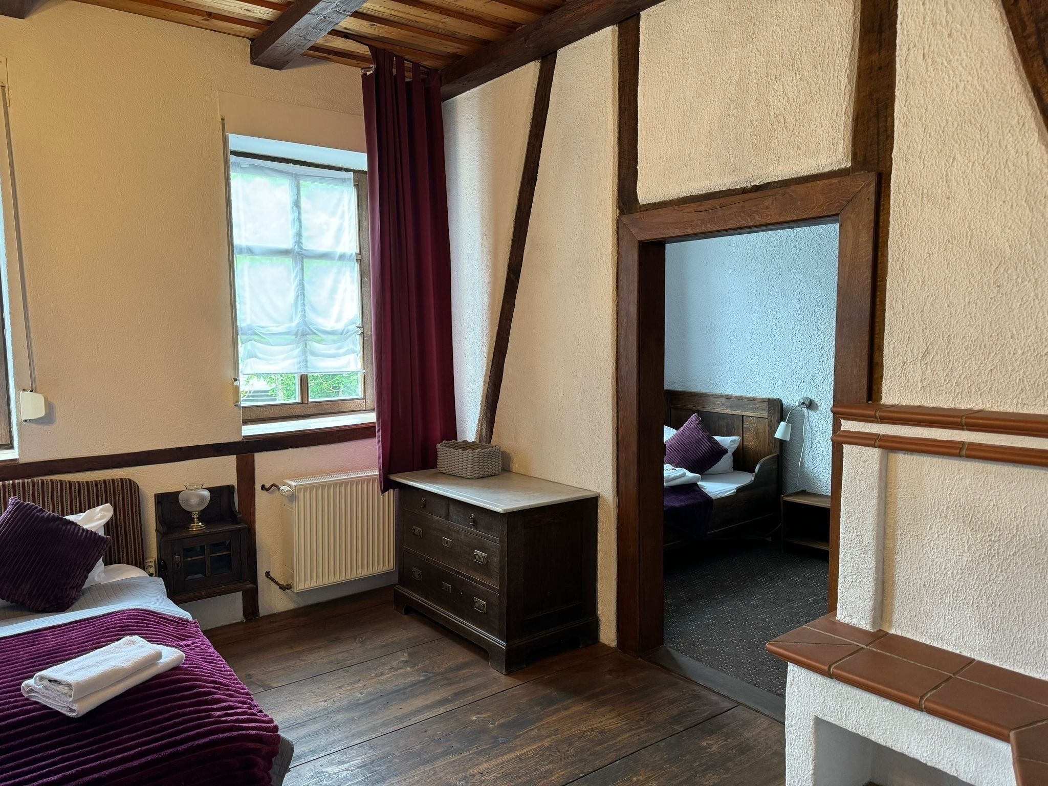 Un dormitorio con cama, cómoda, ventana con cortinas y vista a otra habitación.