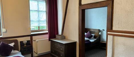 Un dormitorio con cama, cómoda, ventana con cortinas y vista a otra habitación.