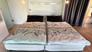 A double bed with floral bedding, a wooden ceiling, and a curtain on the right. - Cozy vacation apartment, fully equipped 80 sqm with garden and underfloor heating (Attendorn)