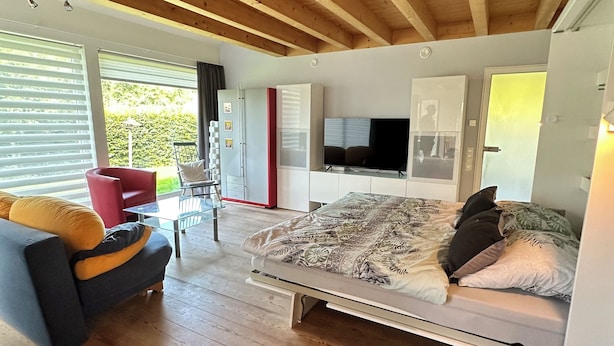 A modern bedroom with a bed, a TV, and a seating area with a red chair and a sofa. - Cozy vacation apartment, fully equipped 80 sqm with garden and underfloor heating (Attendorn)