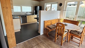 A modern kitchen with wooden beams, a dining area with a wooden table and chairs, and a view of the backyard through large windows. - Cozy vacation apartment, fully equipped 80 sqm with garden and underfloor heating (Attendorn)