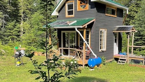 Et toetagers hus med et grønt tag, en overdækket veranda og et lille haveområde med et træ og blomster.