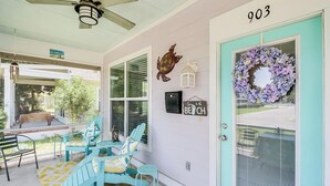 A porch with teal chairs and a yellow patterned rug, a teal door with a wreath, and a number '903' on the wall. - Parrothead Escape-3BD/2BA- 1 block from beach - Pet Friendly (Gulfport)