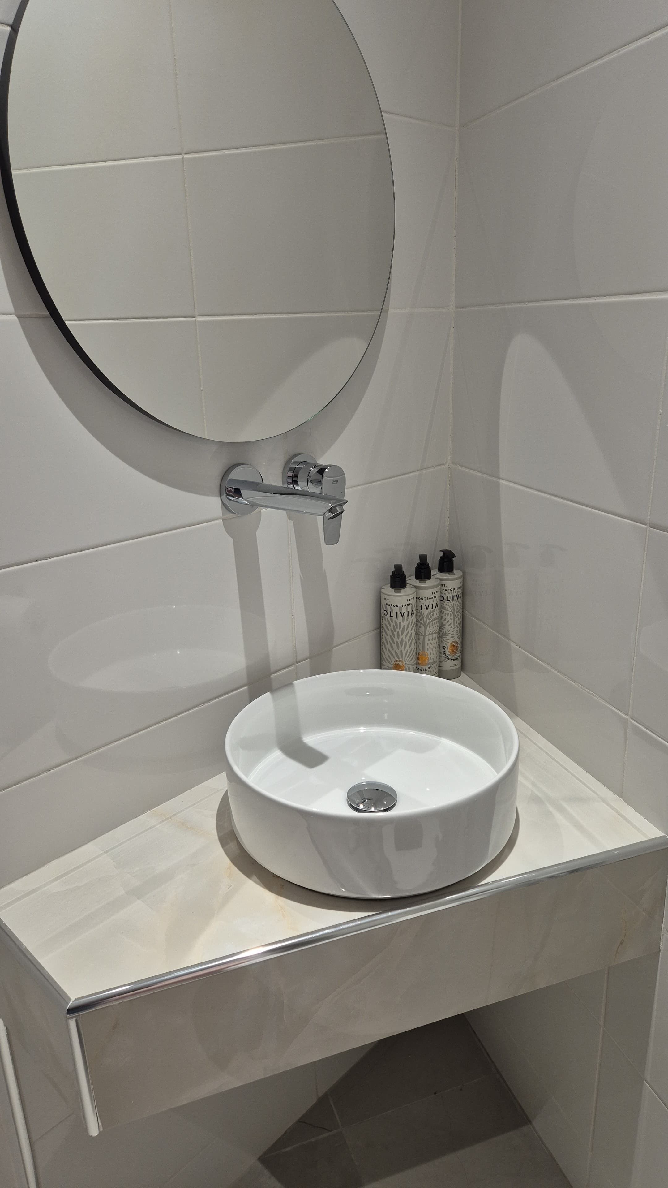 A bathroom with a round mirror, a white sink, and toiletries on the wall.