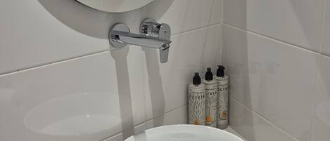 A bathroom with a round mirror, a white sink, and toiletries on the wall.