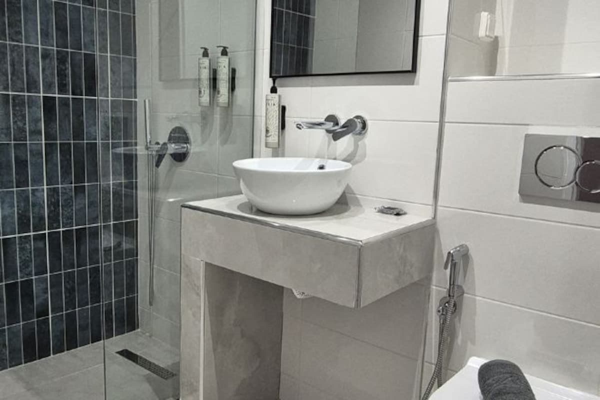 A modern bathroom with a white sink, a glass shower enclosure, and a large mirror above the sink.