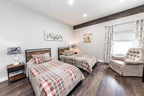 Two single beds with wooden headboards and plaid bedspreads, a plush armchair, and framed artwork adorn this cozy retreat.