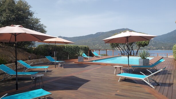 Une terrasse en bois avec une piscine, des chaises longues bleues et des parasols.