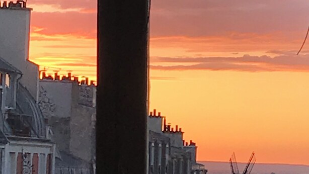 Une vue sur une ville au coucher du soleil, avec des bâtiments se détachant en silhouette sur un ciel aux couleurs éclatantes.