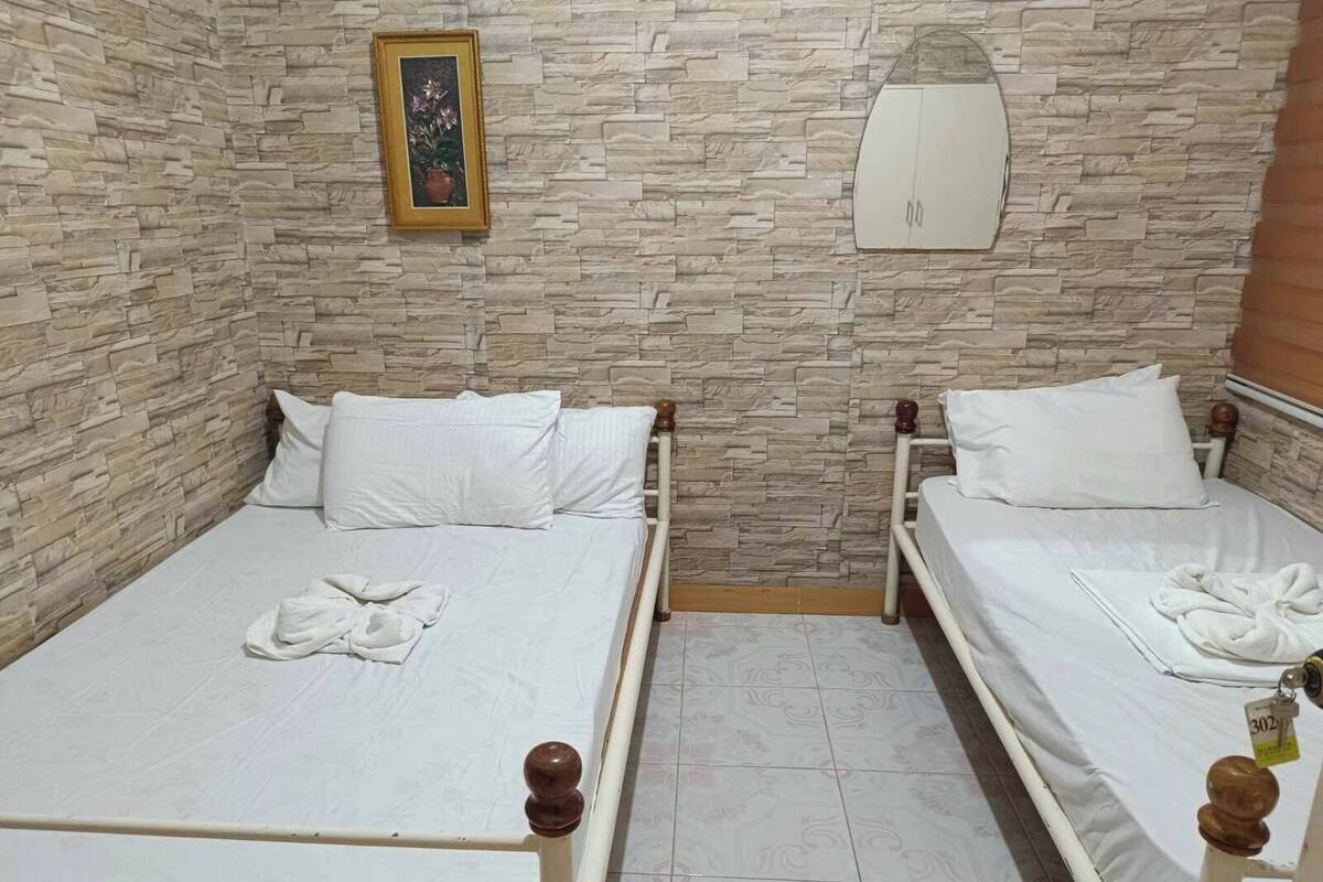 Habitación con dos camas, cada una con sábanas y almohadas blancas, pared con diseño de piedra, un cuadro enmarcado y un armario blanco.