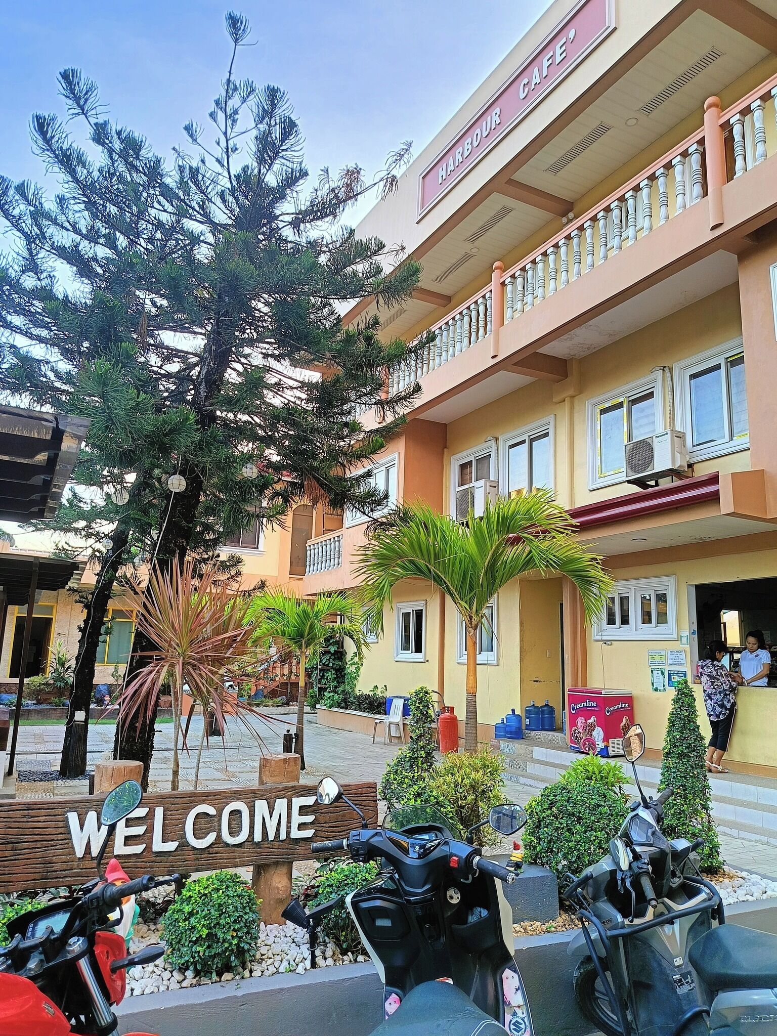 A building with a sign reading "Harbour Cafe" and a "Welcome" sign in front.