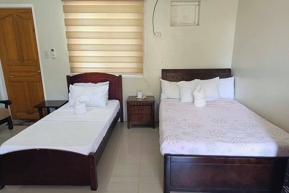 Habitación de hotel con dos camas, un armario de madera, una mesita pequeña y una ventana con persianas.