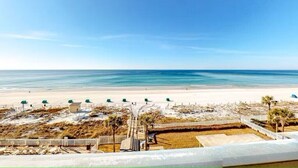 Strandudsigt med sandet bredde, en lille bygning og et afspærret område med palmer.