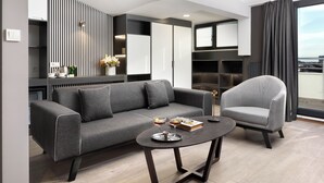 Een moderne woonkamer met een grijze bank, een rond bijzettafeltje met drankjes, een gestreept fauteuil en een uitzicht op de stad door grote ramen.