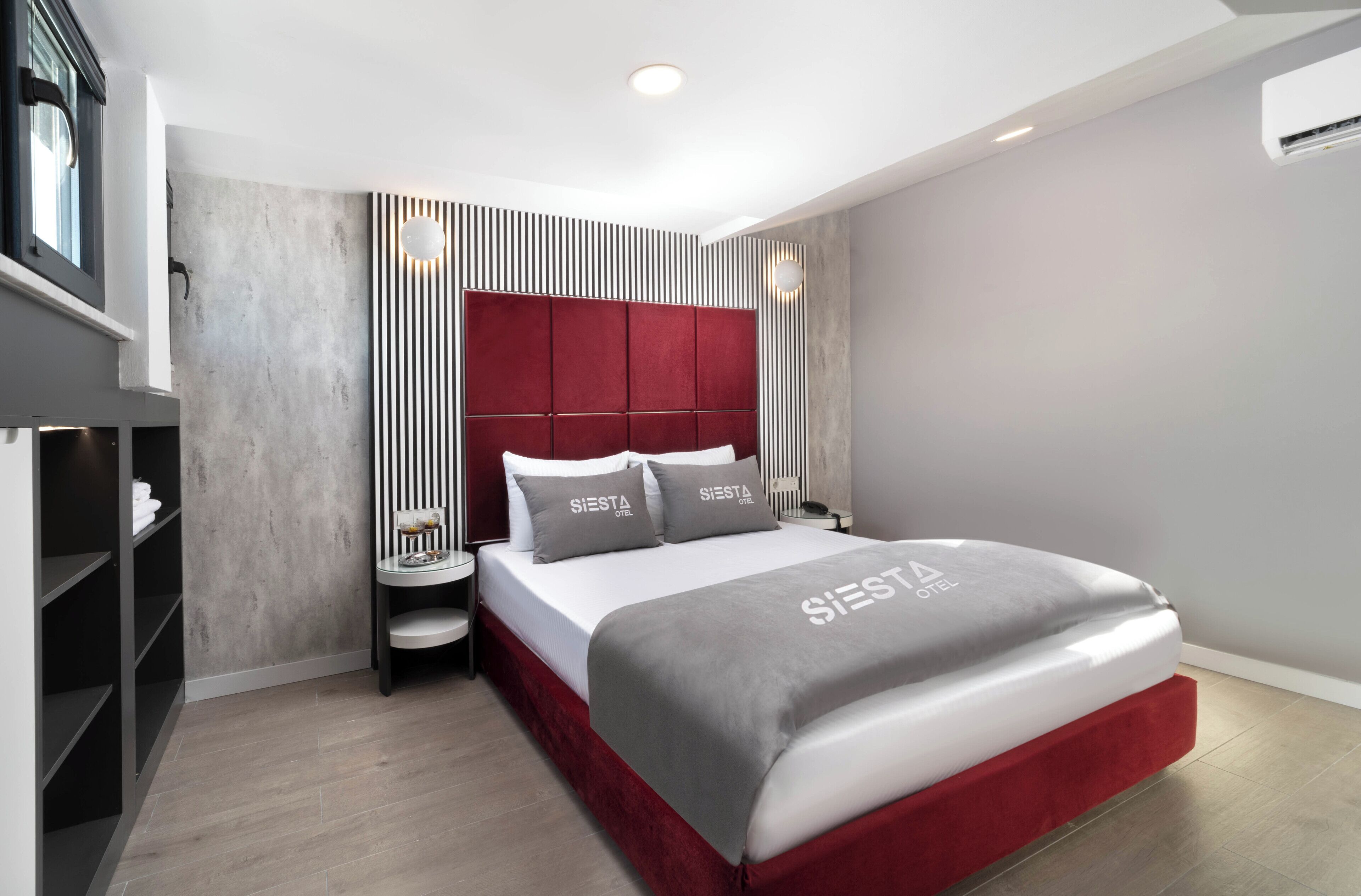 A modern hotel room with a large bed, a bedside table, a wardrobe, and a built-in shelf unit.