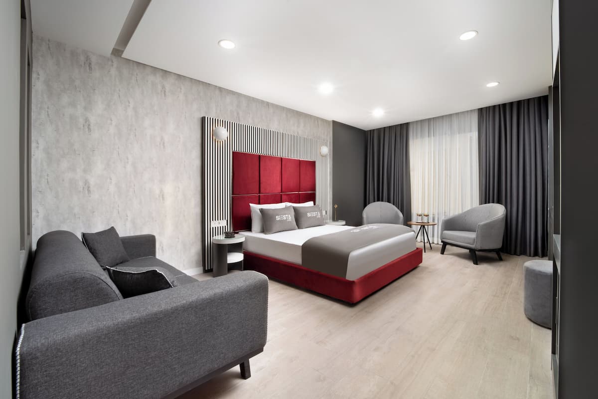 Una habitación de hotel moderna con una cama grande, un sofá gris, una mesita peque ña y una silla.