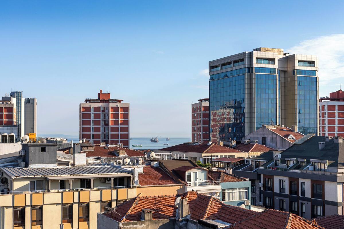 Un paisaje urbano con una mezcla de edificios modernos y tradicionales, incluyendo un rascacielos de vidrio destacado y varias estructuras más pequeñas con tejados de tejas rojas.