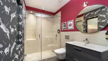 Un baño moderno con cabina de ducha de vidrio, inodoro blanco, tocador con espejo y paredes con estampado de cebra.