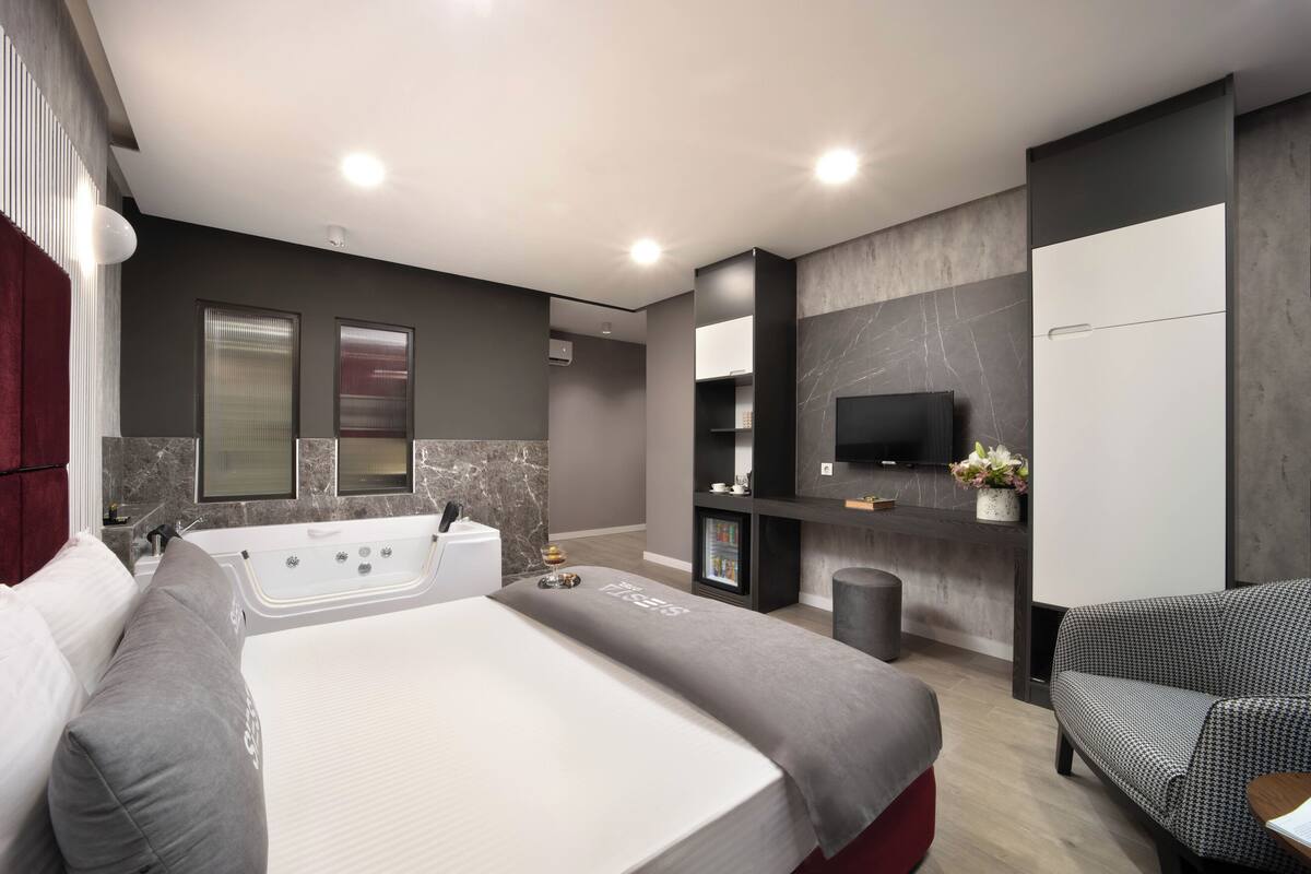 Una habitación de hotel moderna con una cama grande, una zona de estar, un televisor y un minibar.