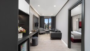 Een moderne hotelkamer met een bank, een tafeltje, een televisie en een raam met gordijnen.