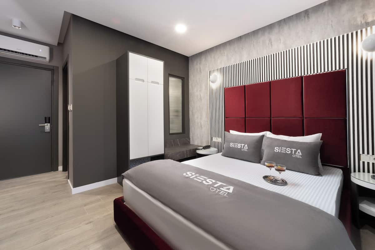 Una habitación de hotel moderna con una cama grande, cabecera roja y minibar.