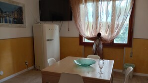 A dining area with a table, chairs, a television, and a refrigerator. - Adam Venice 1 (Mira)