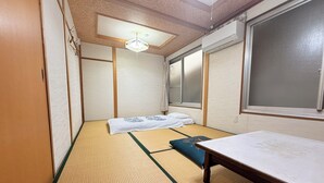 A traditional Japanese room with tatami flooring, a low table, and a bed with a blue cushion.