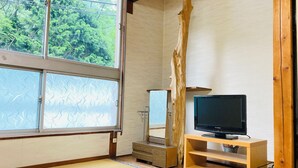 A traditional Japanese room with tatami flooring, a television on a wooden stand, and a large window with frosted glass.