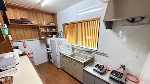 A compact kitchen with a refrigerator, stove, sink, and wooden shelves.