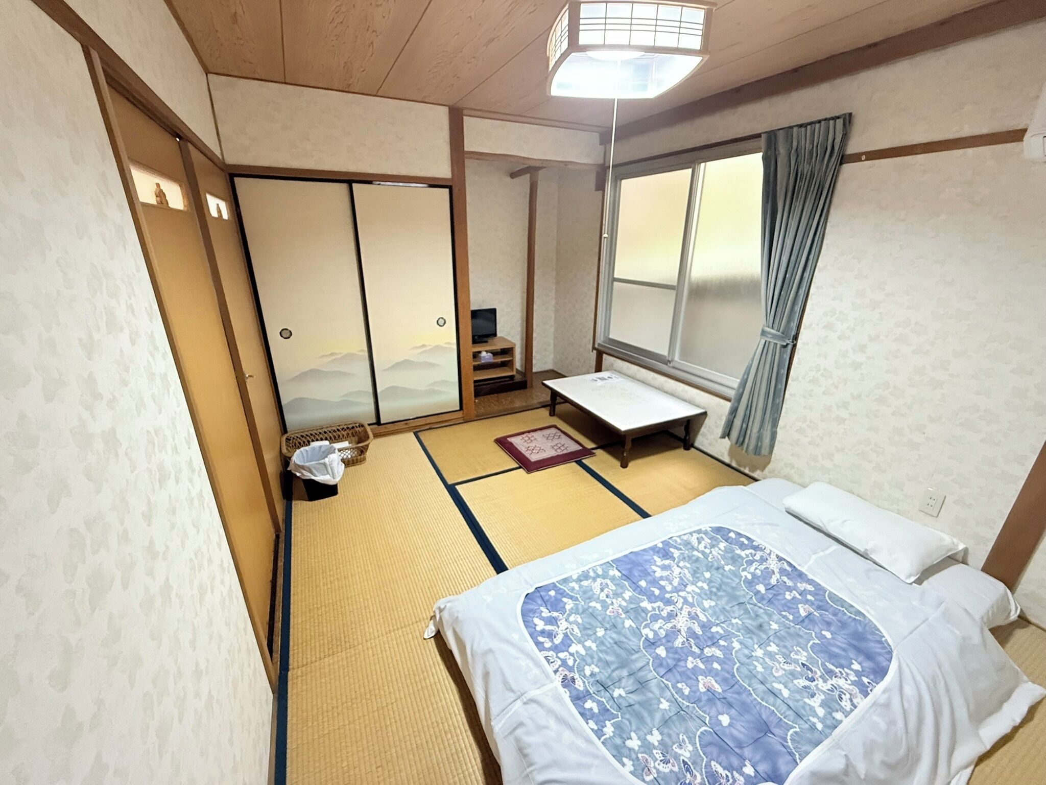 A traditional Japanese room with tatami flooring, a futon bed, sliding doors, and a view of the mountains through a window.
