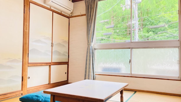 A traditional Japanese room with tatami flooring, a shoji screen, a wooden table, and a view of greenery outside.