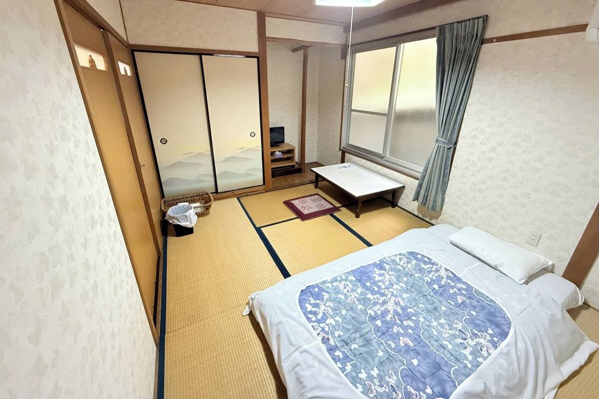 A traditional Japanese room with tatami flooring, a futon bed, sliding doors, and a view of the mountains through a window.