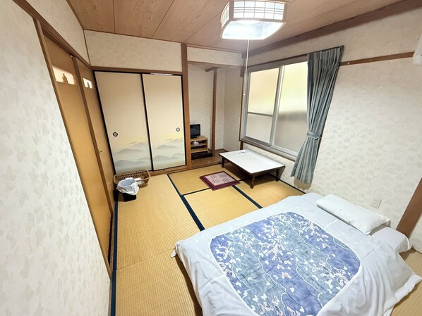 A traditional Japanese room with tatami flooring, a futon bed, sliding doors, and a view of the mountains through a window.