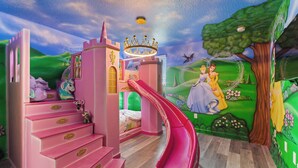 Ett lekrum för barn med ett rosa slott, en rutschkana och en väggmålning med prinsessor.