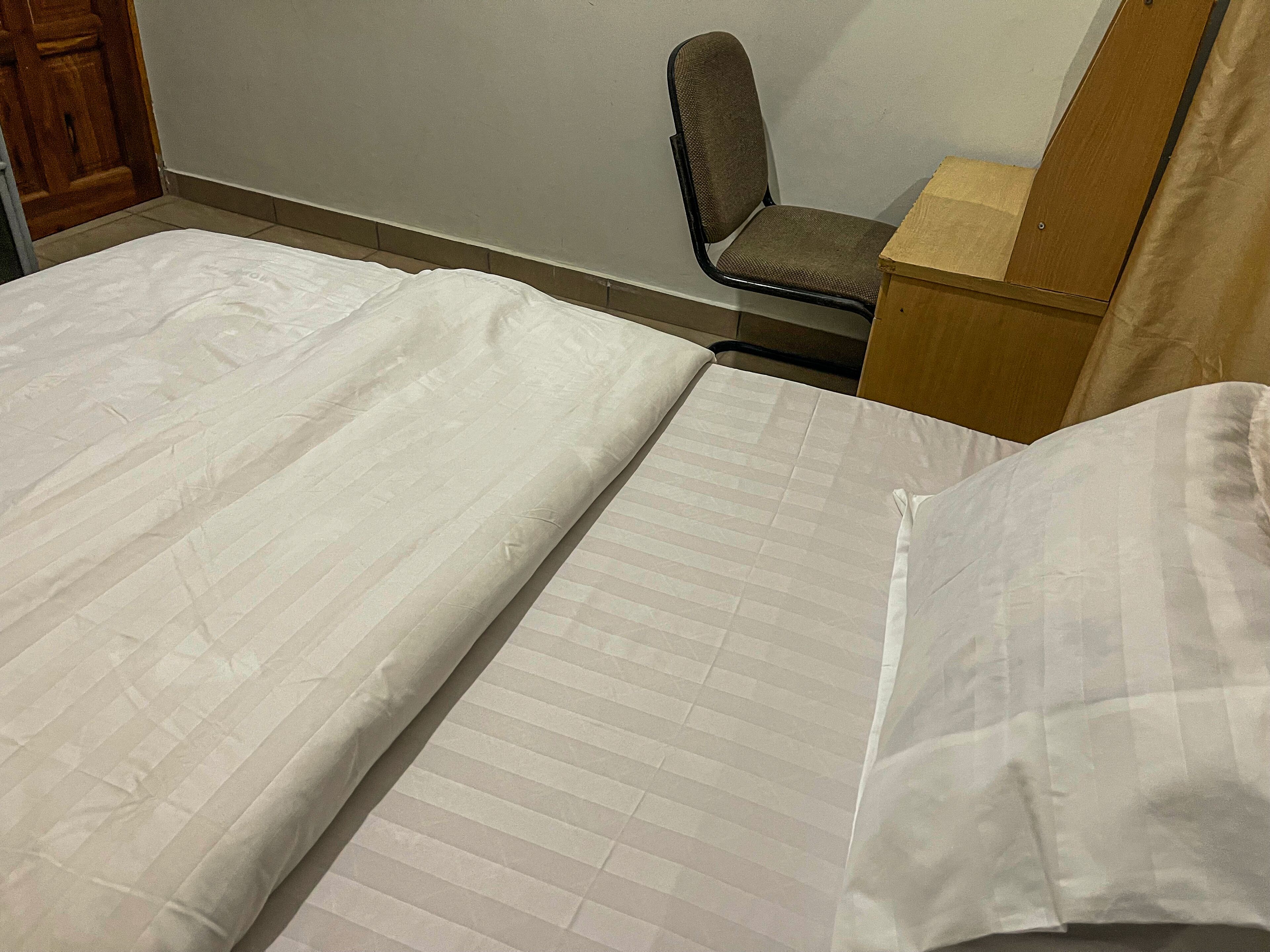 A hotel room with two beds, a wooden nightstand, and a chair.
