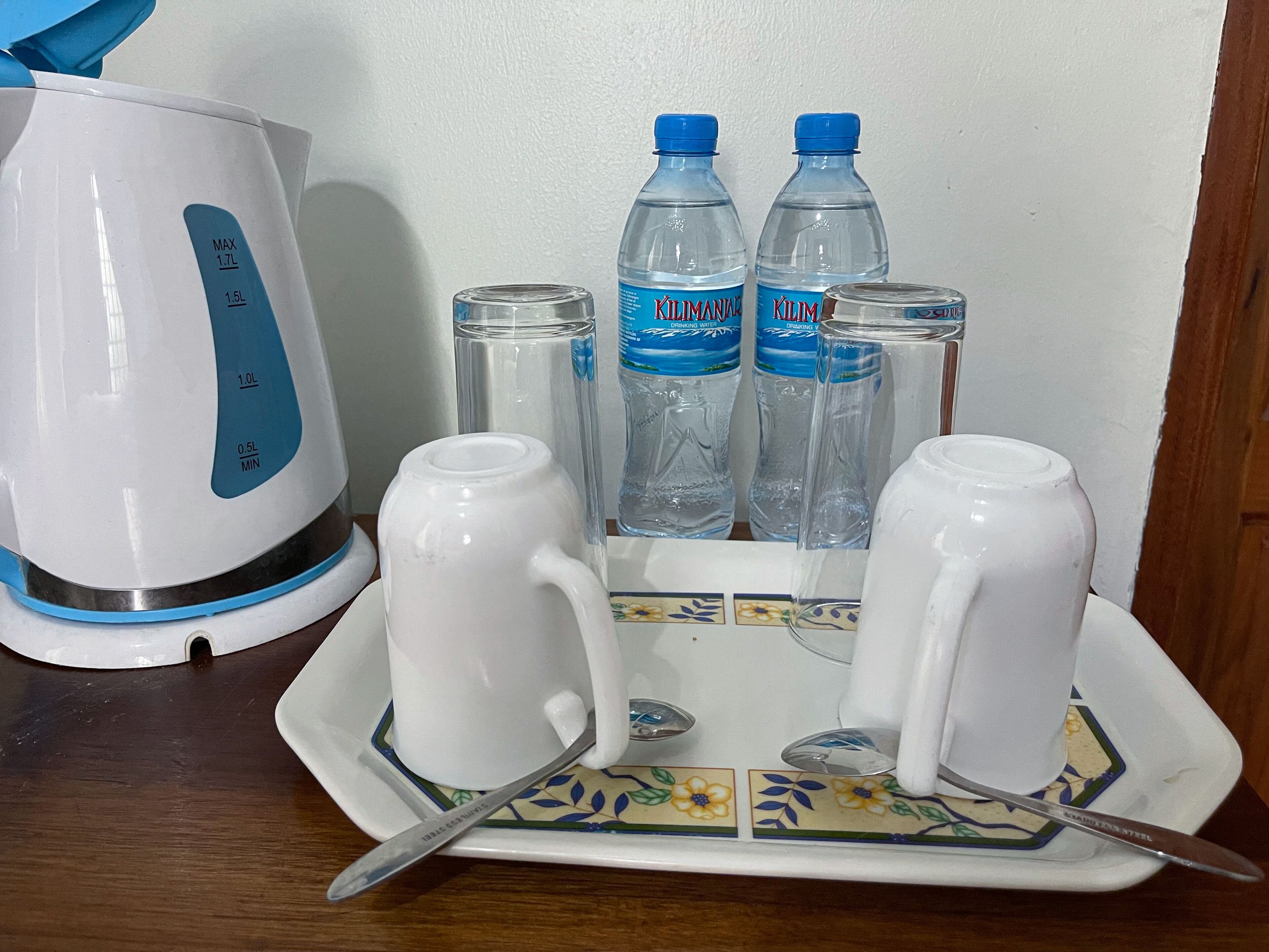 A kitchen setup with a white kettle, two water bottles, and two white mugs on a tray.